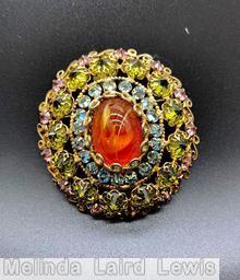 Schreiner 3 rounds radial oval domed radial pin large oval cab center 19 surrounding small inverted stone 2nd round 13 inverted stone outer round 13 stone scrollwork small circle style prong swirled carnelian large oval cab center clear aqua small inverted stone olivine inverted stone clear pink small inverted stone goldtone jewelry