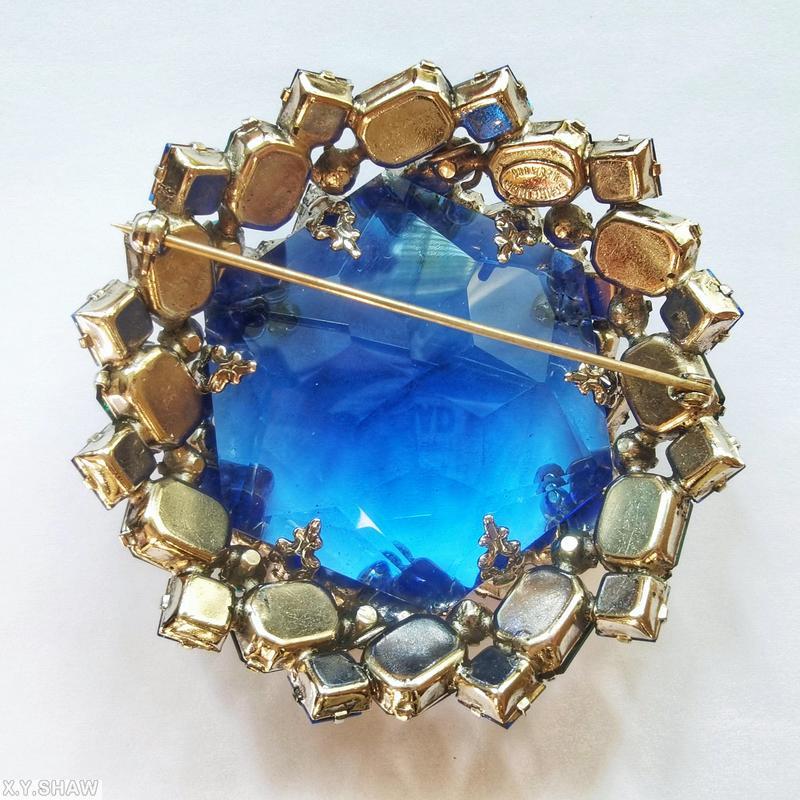 Schreiner large faceted open back center domed round pin 8 waves of seeds 16 oval stone side clear navy hexagonal faceted crystal center purple inverted square stone aqua clear faceted baguette opaque baby blue small chaton emeral colored emerald cut stone goldtone jewelry