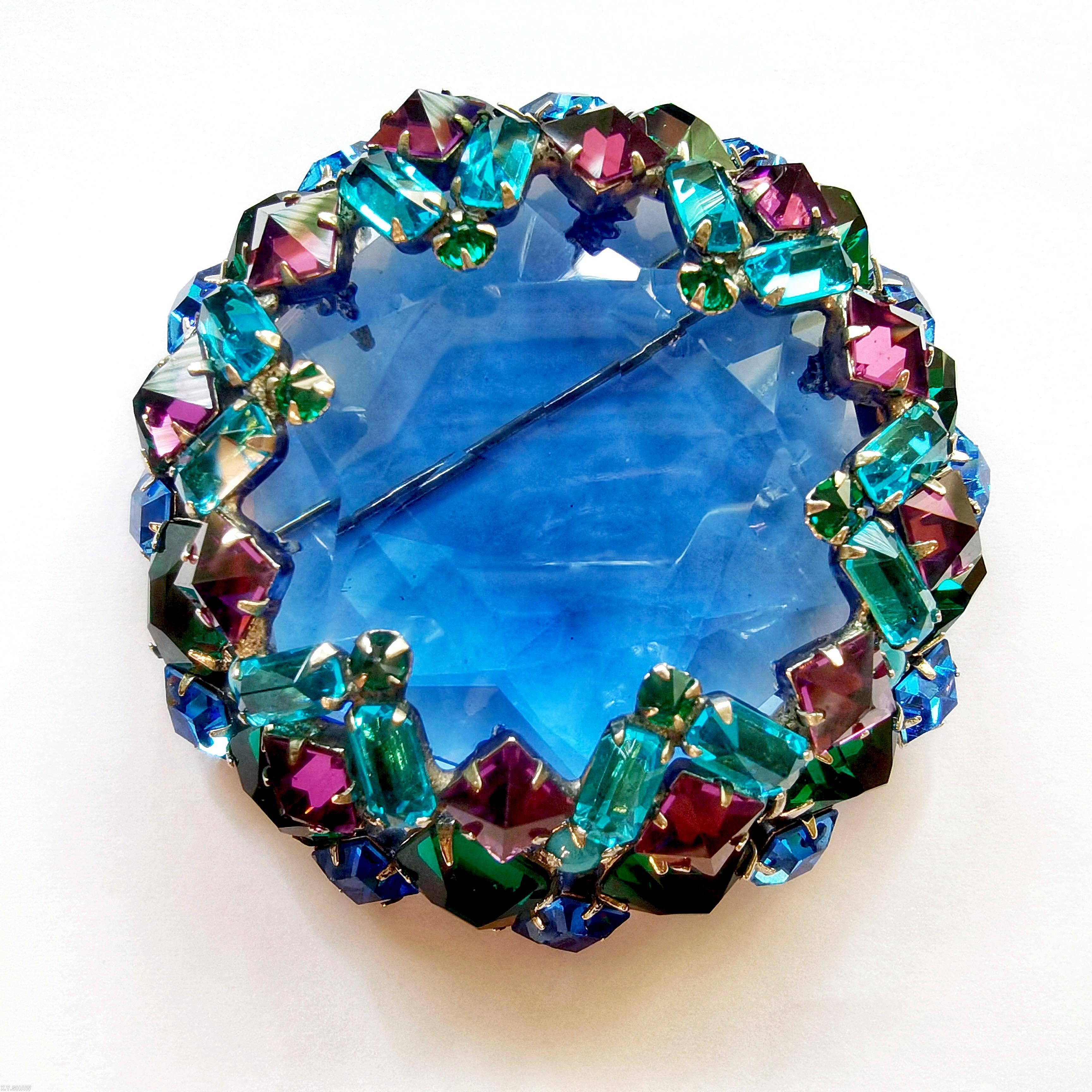 Schreiner large faceted open back center domed round pin 8 waves of seeds 16 oval stone side clear navy hexagonal faceted crystal center purple inverted square stone aqua clear faceted baguette opaque baby blue small chaton emeral colored emerald cut stone goldtone jewelry