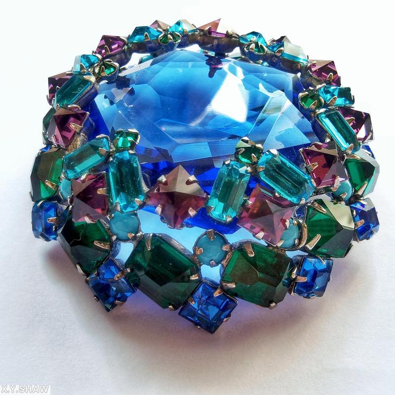 Schreiner large faceted open back center domed round pin 8 waves of seeds 16 oval stone side clear navy hexagonal faceted crystal center purple inverted square stone aqua clear faceted baguette opaque baby blue small chaton emeral colored emerald cut stone goldtone jewelry